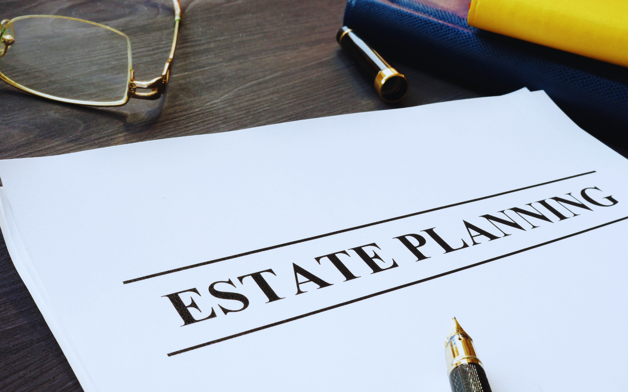Photo of a paper that reads "estate planning" with a pen and glasses nearby.
